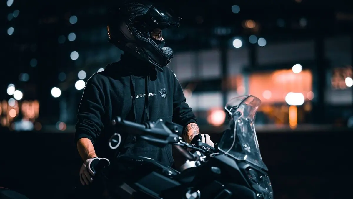 Motard urbain relevant la mentonnière de son casque modulable à un feu rouge, circulation dense